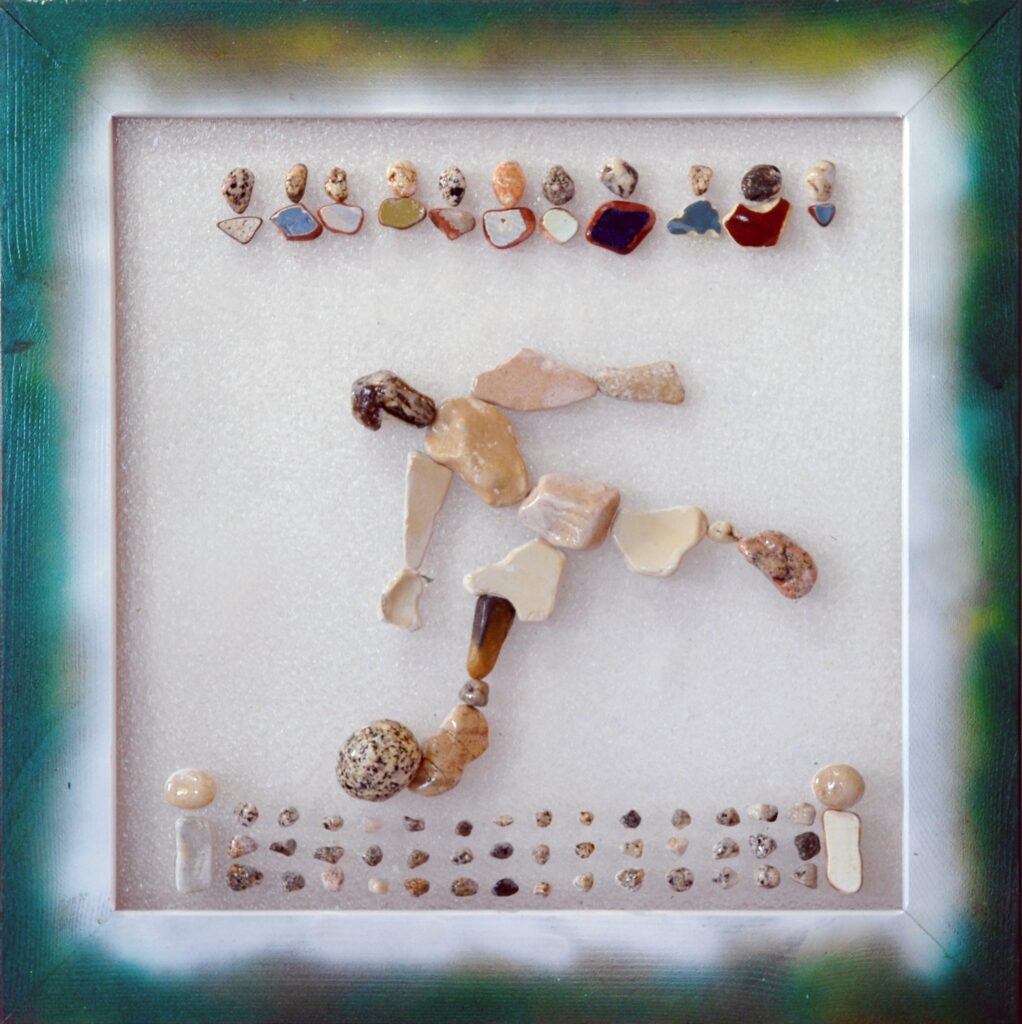 Calciatore realizzato con pietre naturali e frammenti ceramici su plexiglas mentre controlla il pallone durante una partita, sotto lo sguardo degli spettatori.