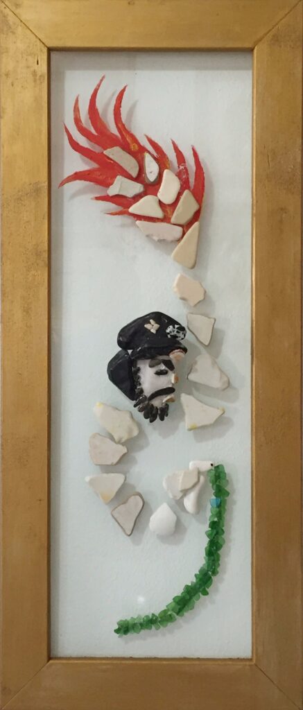 Rappresentazione simbolica di Ernesto Che Guevara realizzata con pietre, frammenti ceramici e vetro marino su vetro, accompagnata da una fiamma rossa e da una linea curva verde.