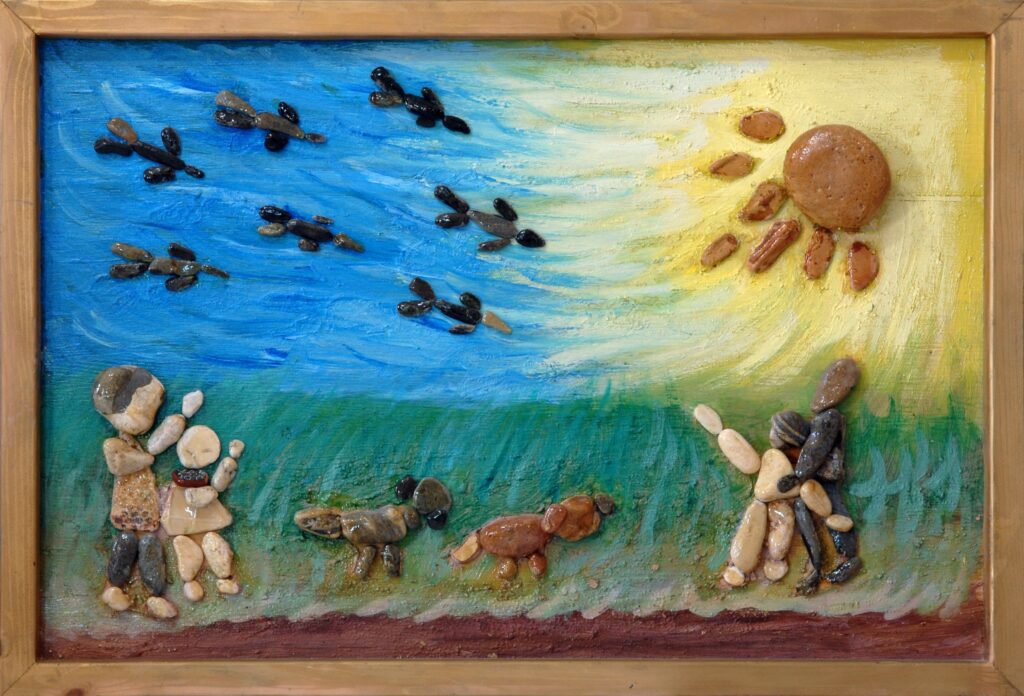 Escena familiar realizada con piedras naturales que muestra aves en vuelo, una madre con su hijo, un padre con un niño y dos perros bajo un sol radiante.