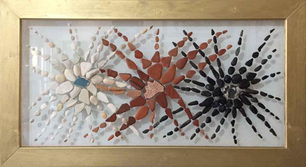 Composizione astratta realizzata con pietre marine e frammenti di ceramica su plexiglas che rappresenta tre stelle o fiori radianti nei toni del bianco, del rosso e del nero.