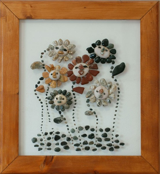 Flores con rostros sonrientes realizadas con piedras naturales sobre plexiglás, formando una composición alegre y decorativa.