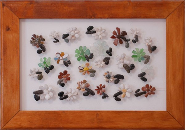 Pequeñas flores realizadas con piedras naturales de distintos colores sobre plexiglás, distribuidas en una composición decorativa y armoniosa.