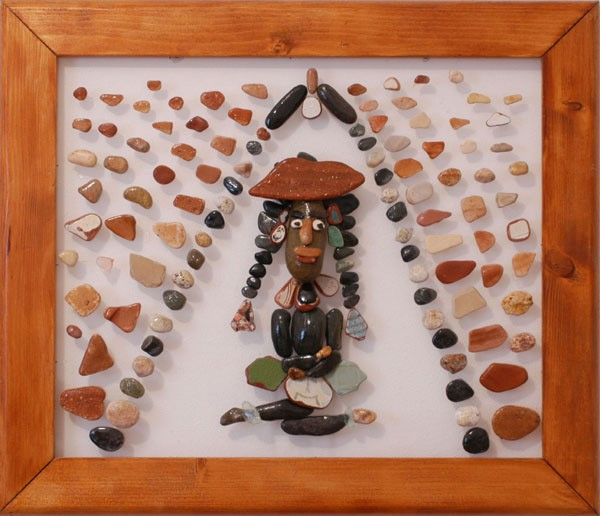Figura femenina inspirada en una mujer indígena, realizada con piedras naturales sobre plexiglás y rodeada por una composición decorativa de pequeñas piedras.