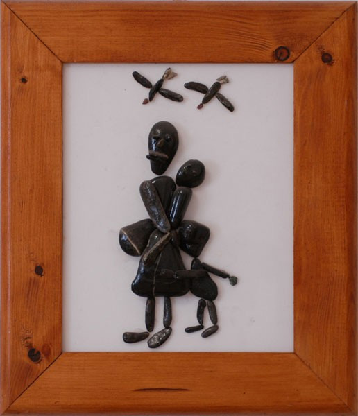 Figura de una madre y un niño representados con piedras oscuras sobre plexiglás, bajo dos aves que vuelan en el cielo.